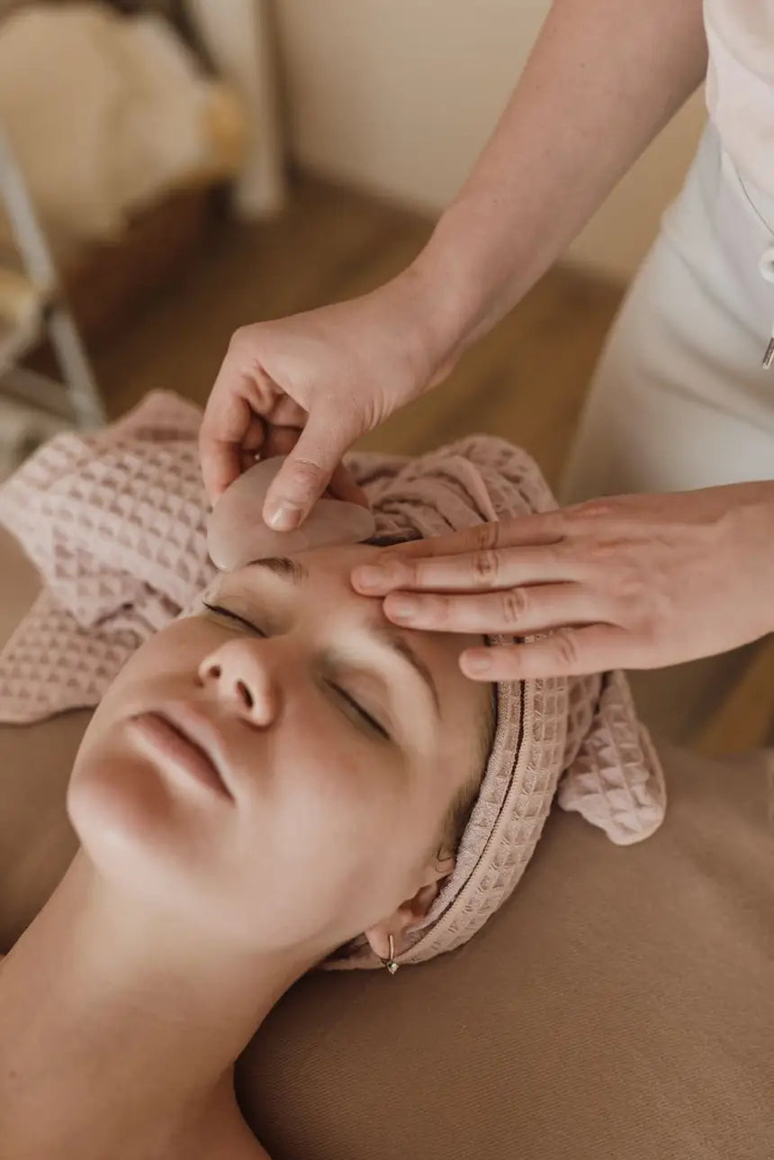 Facialist performing a gua sha facial massage with a stone tool