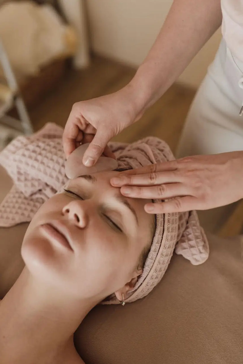 Facialist performing a gua sha facial massage with a stone tool